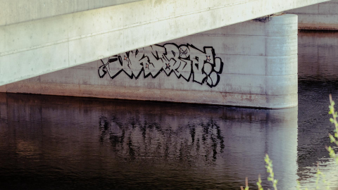 graffiti under a bridge reflecting on water